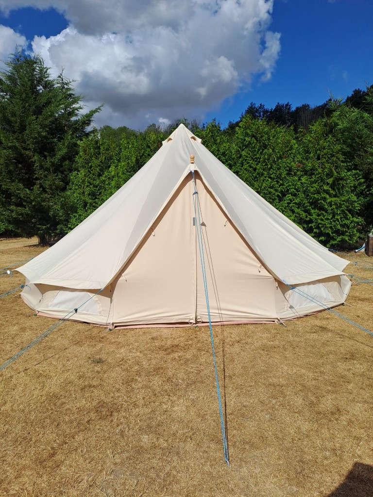 Canvas bell tent pitched on grass under a clear sky
