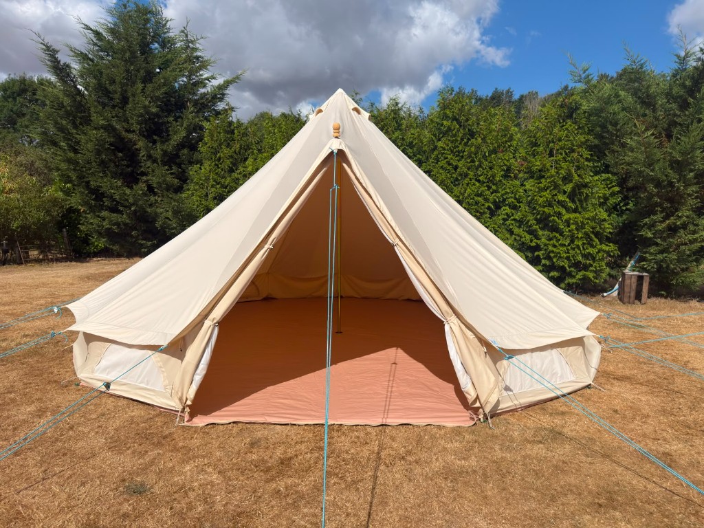 Cream canvas bell tent pitched on grass against trees and blue sky