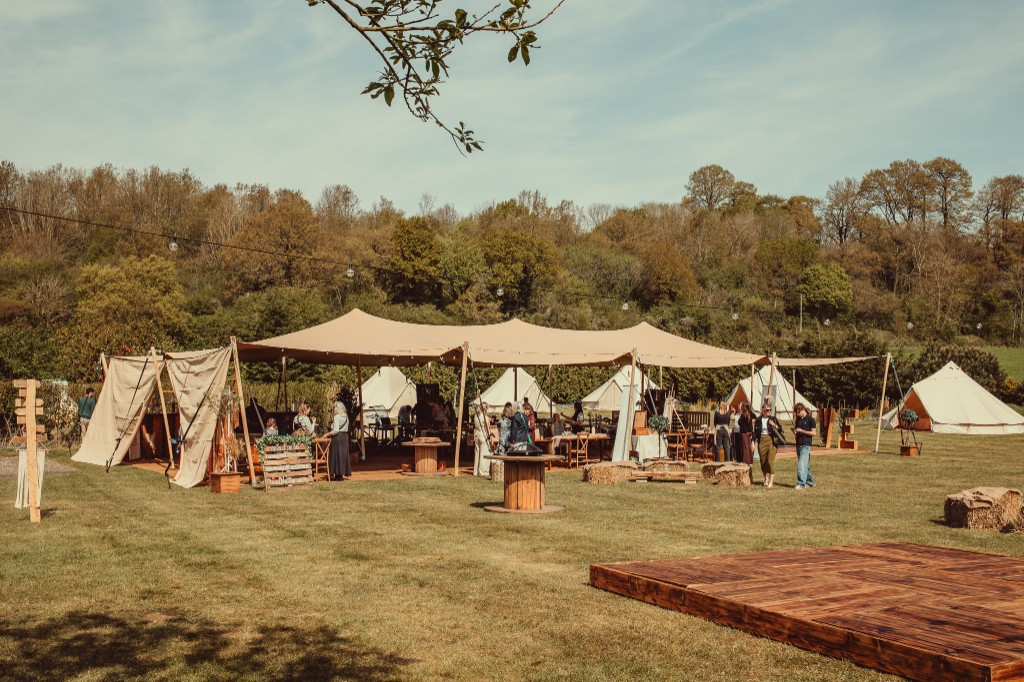 Open stretch tent with dance floor, festoon lighting and bell tents beyond