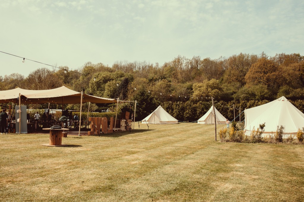 Woodhill stretch tent and cream bell tents set up across a green lawn for an outdoor celebration